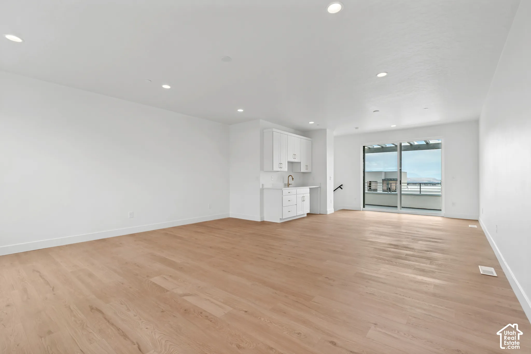 Expansive living area featuring light wood-finish flooring, recessed lighting, and a built-in wet bar with white cabinetry