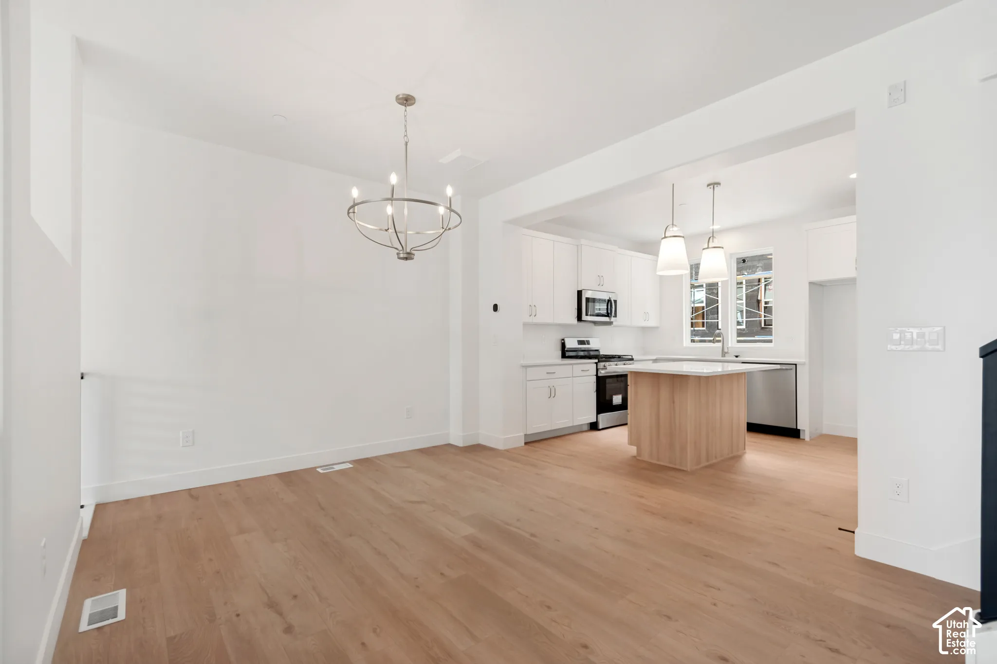 Light wood-finish flooring throughout, bright white walls, and a modern kitchen featuring stainless steel appliances, white cabinetry, and an island with pendant lighting