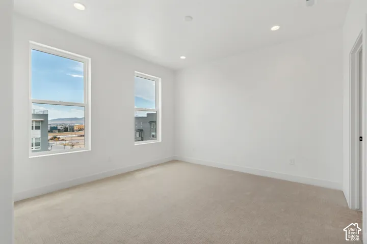 Neutral-toned carpeting, recessed ceiling lighting, and two large windows with white trim