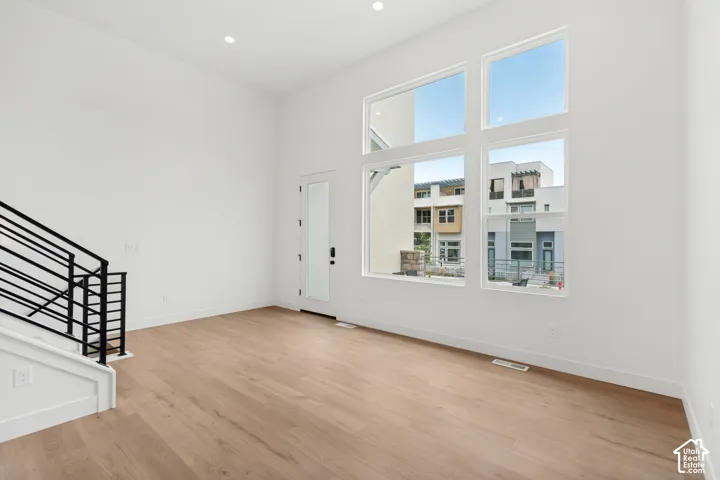 Expansive windows, light wood-finish flooring, recessed lighting, and a modern metal stair railing
