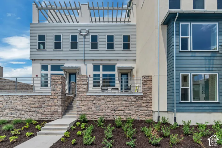 Contemporary multi-level exterior with a stone-clad retaining wall, horizontal siding, and a rooftop pergola