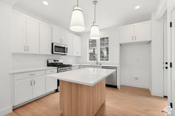Modern kitchen featuring light wood-finish flooring, white cabinetry, stainless steel appliances, a center island with a light-toned countertop, and recessed lighting