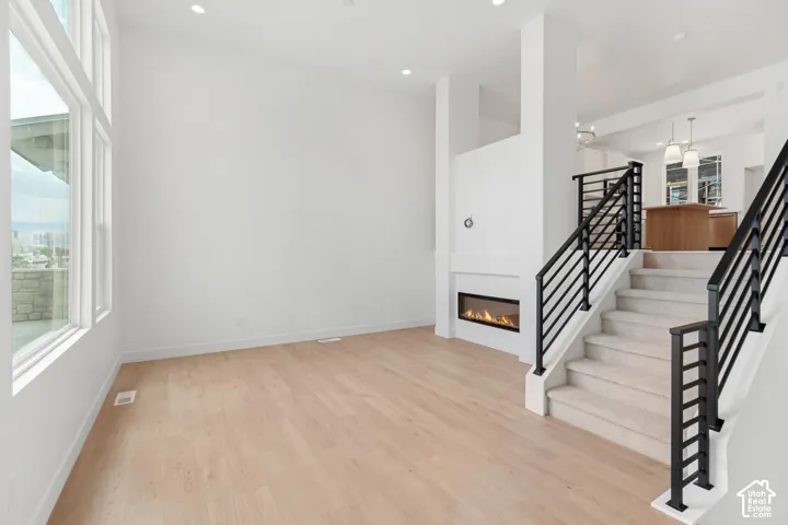 Wood-finish flooring, linear fireplace, white walls, and a multi-level staircase with black iron railings