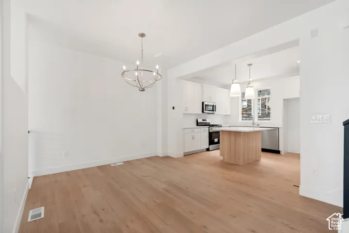 Light wood-finish flooring throughout, bright white walls, and a modern kitchen featuring stainless steel appliances, white cabinetry, and an island with pendant lighting