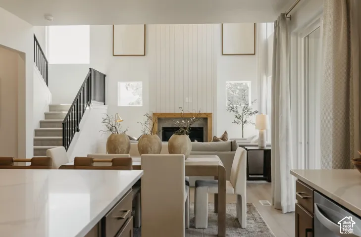 Open-concept living space featuring a high-vaulted ceiling, shiplap-accented fireplace, wood-finish flooring, and a carpeted staircase with black railings
