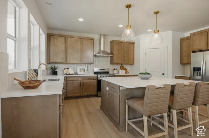 Kitchen featuring a central island with countertop seating, wood-finish cabinetry, stainless steel appliances, and light wood-finish flooring