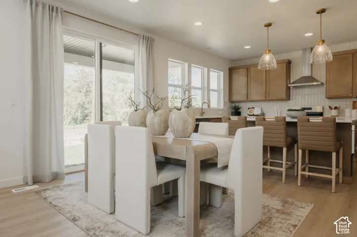 Open-concept living space with wood-finish flooring, a kitchen featuring wood cabinetry and a tile backsplash, and a dining area with pendant lighting