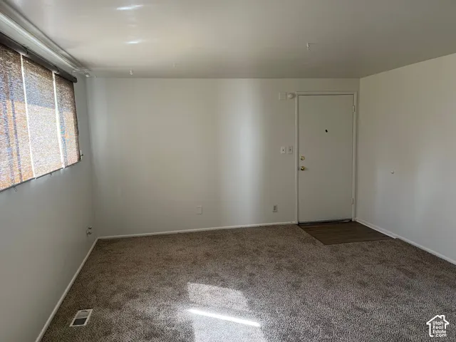 Carpeted flooring extending throughout, white painted walls, and a solid entry door with brass hardware
