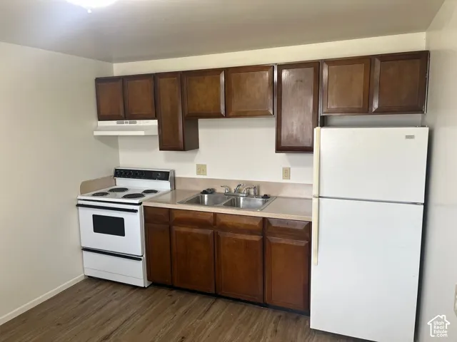 Kitchen featuring wood-finish flooring, dark wood cabinetry, white appliances, a double basin sink, and laminate countertops