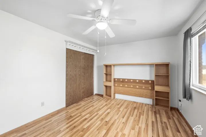 Hardwood-finish flooring, a ceiling fan with integrated lighting, and a window with natural light