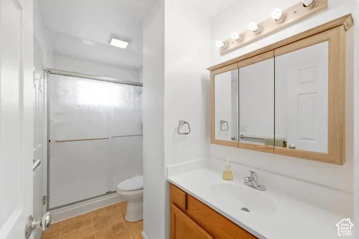 Bathroom featuring a white vanity with a single basin sink, a multi-panel mirrored medicine cabinet, a shower enclosure with sliding glass doors, and brown tile flooring