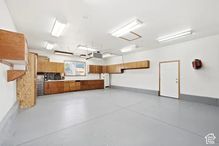 Spacious garage with light gray concrete flooring, extensive wood cabinetry, and a built-in workbench