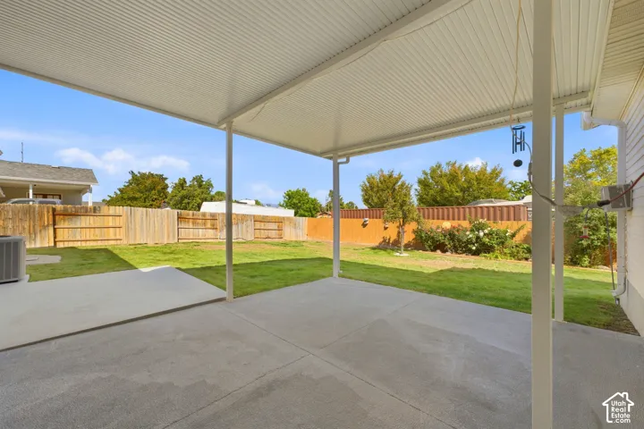 Covered patio with concrete surface, extending to a grassy yard featuring a wood fence and mature landscaping