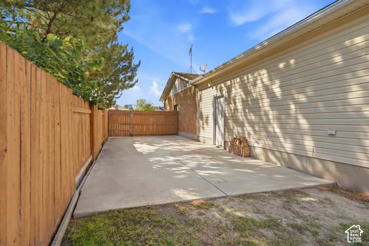Concrete patio space with a wooden privacy fence, a wooden fence gate, and vinyl siding