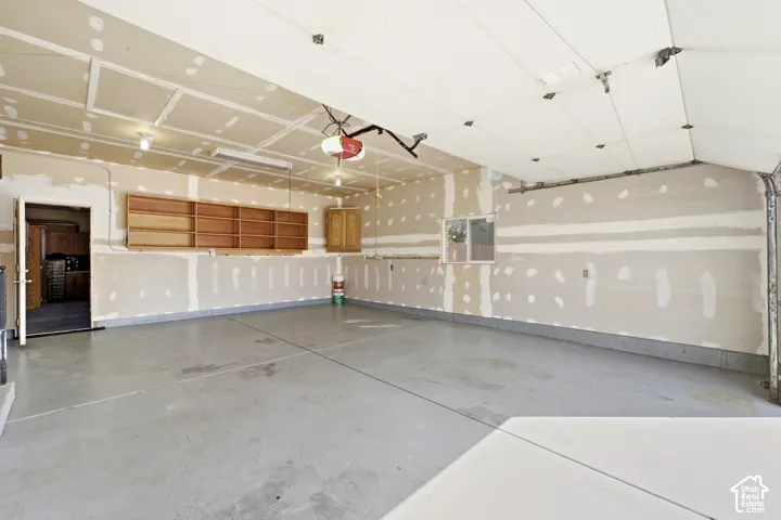 Spacious garage with concrete flooring, built-in wooden shelving, overhead lighting, and a single window