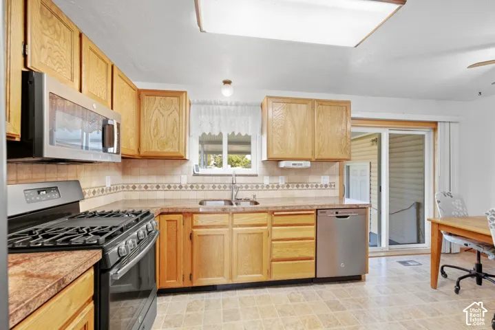 Kitchen featuring light wood cabinetry, stainless steel appliances, patterned tile backsplash, and a sliding glass door