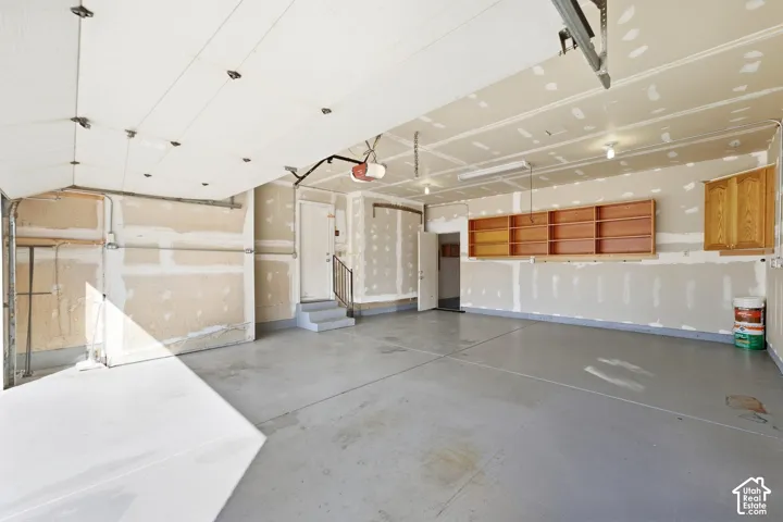 Concrete flooring, built-in shelving, two-stall garage door mechanism, interior access door, and overhead lighting