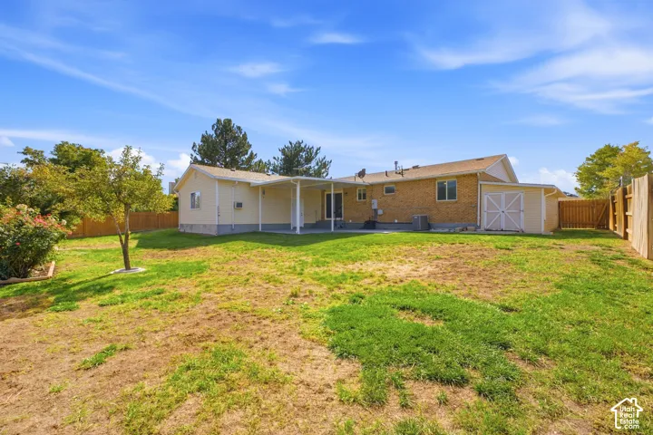 Expansive backyard with a covered patio, brick exterior, and a detached storage shed