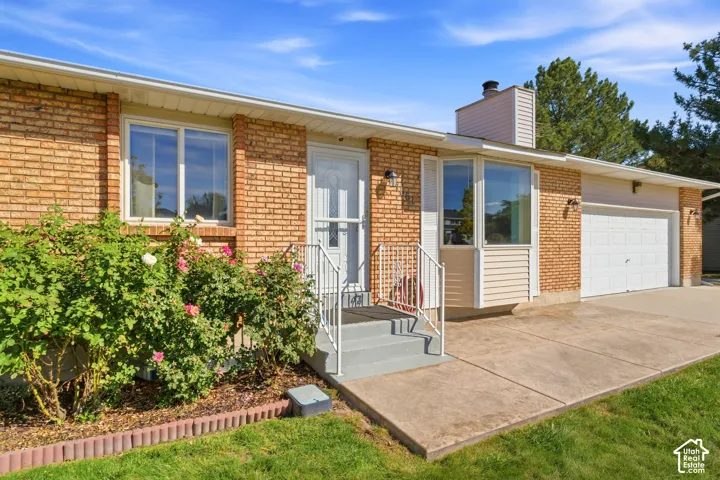 Brick exterior featuring a two-car garage, a bay window, and mature landscaping