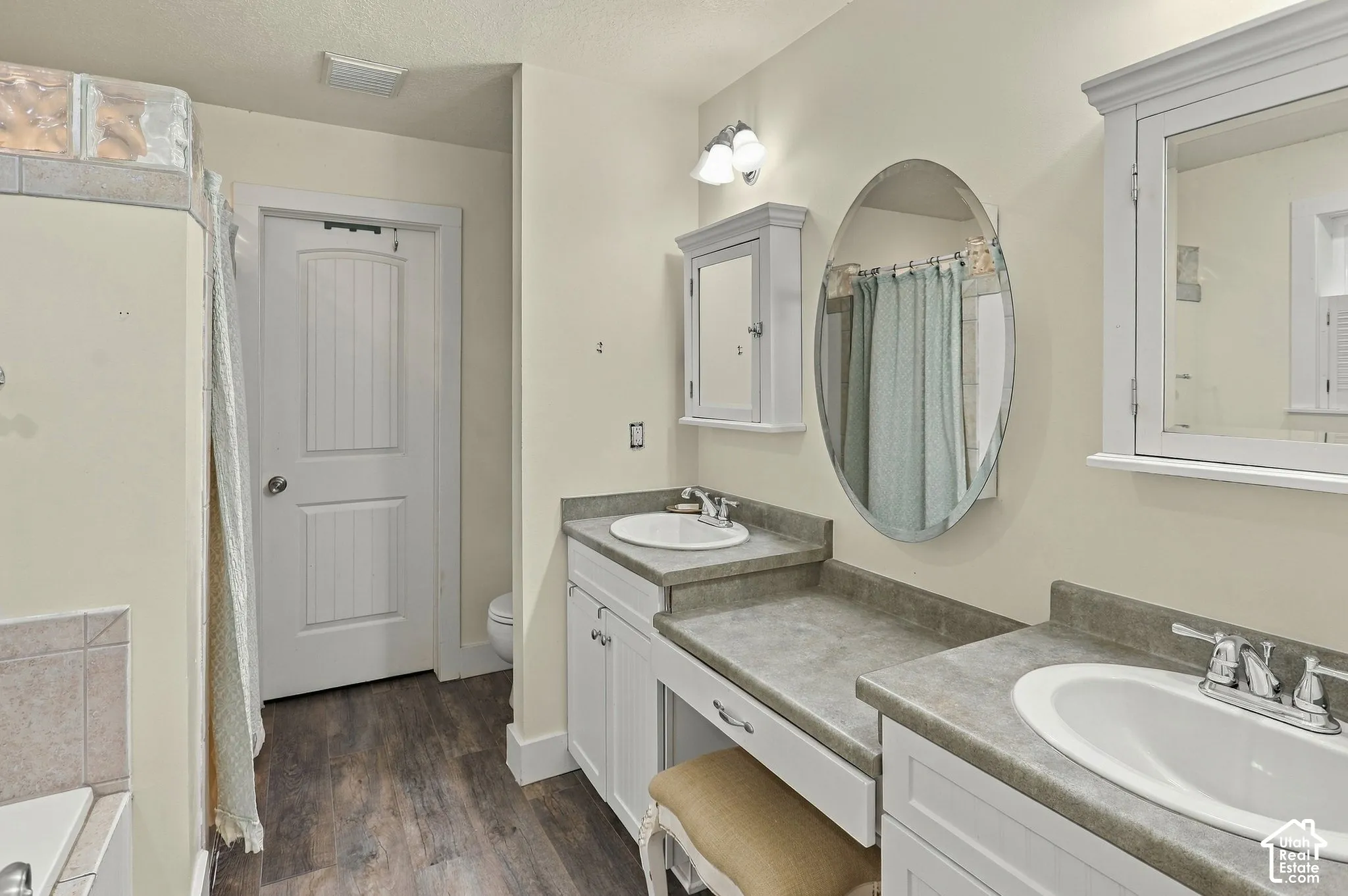 Dual sink vanity with white cabinetry and grey countertops, wood-finish flooring, and wall-mounted medicine cabinets