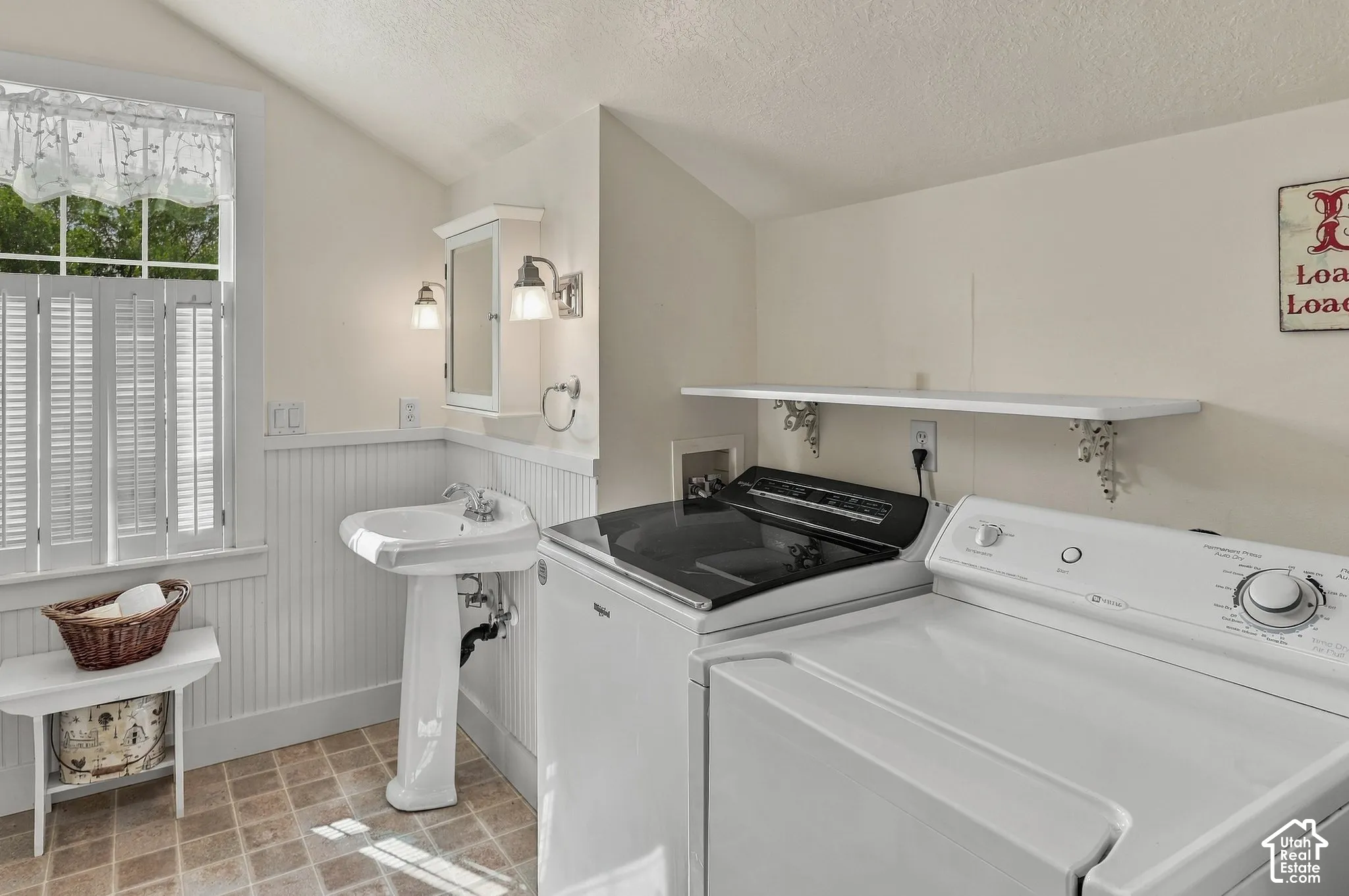 Pedestal sink, wall-mounted medicine cabinet with sconces, white beadboard wainscoting, louvered window shutters, and tiled flooring