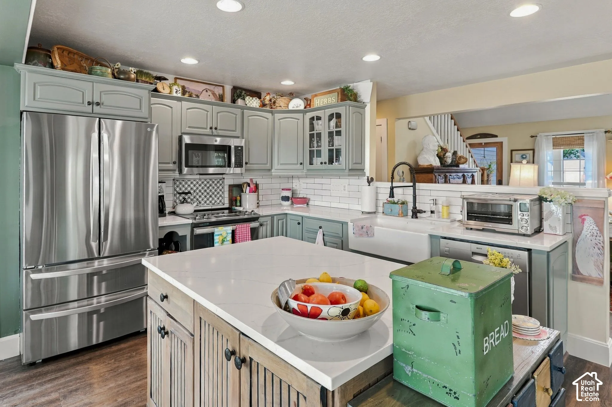 Kitchen featuring light gray cabinetry, stainless steel appliances, a white farmhouse sink, and a center island with a white countertop