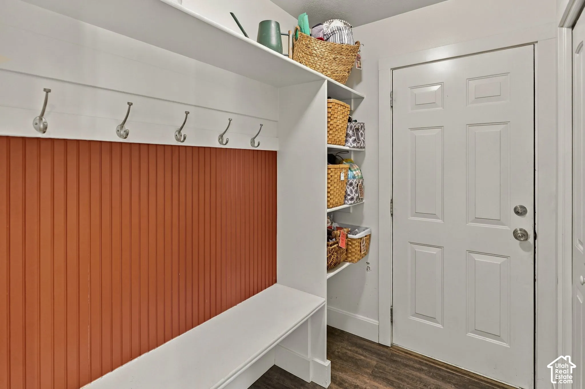 Built-in storage bench with an accent paneled wall, wall-mounted coat hooks, and overhead shelving