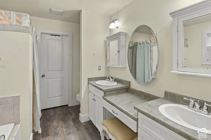 Dual sink vanity with white cabinetry and grey countertops, wood-finish flooring, and wall-mounted medicine cabinets