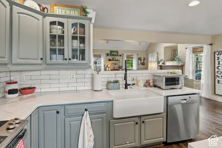 Kitchen featuring light gray cabinetry, white subway tile backsplash, white farmhouse sink, stainless steel dishwasher, and light-colored countertops