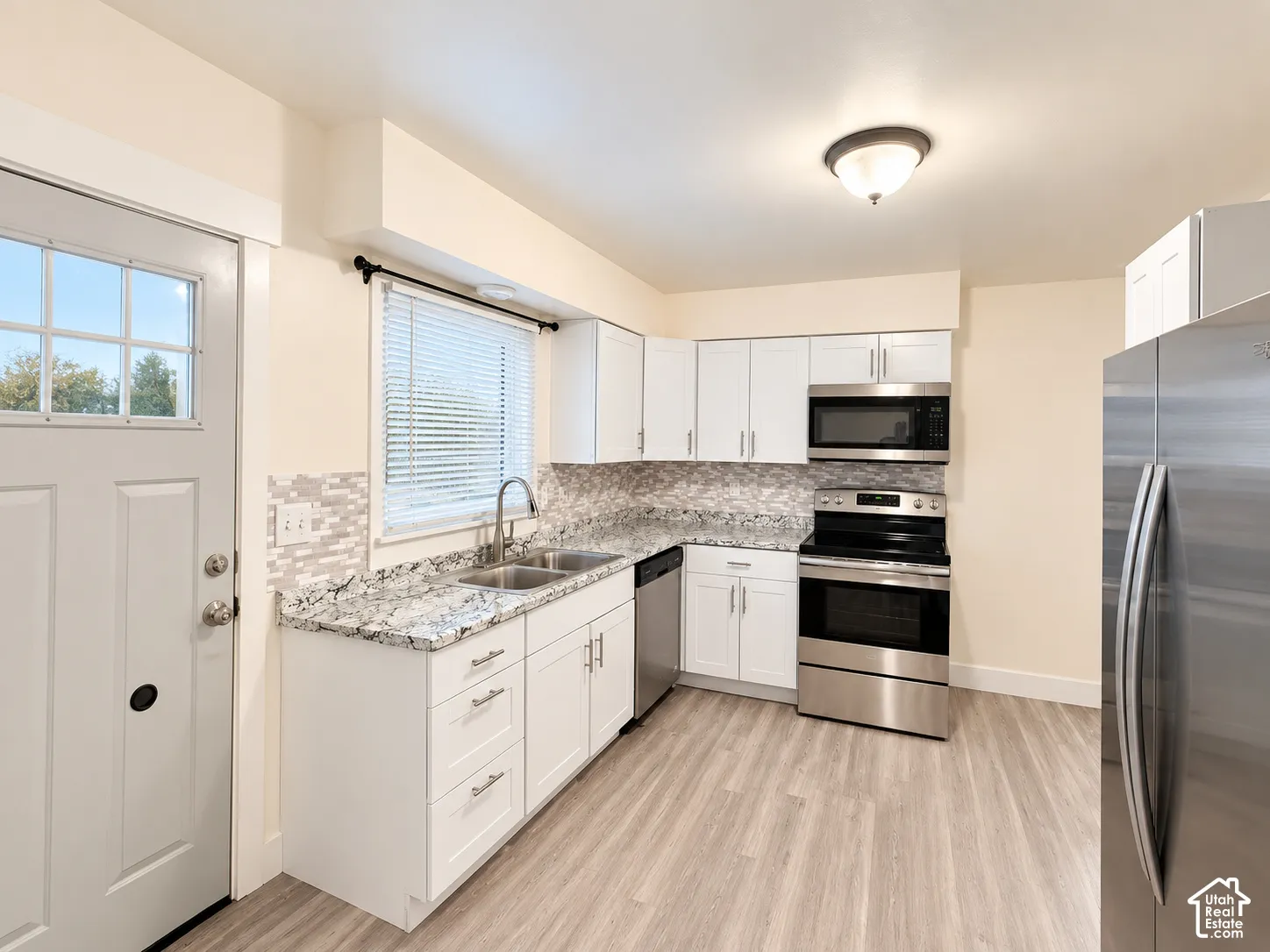 Kitchen featuring white shaker-style cabinetry, stone-finish countertops, mosaic tile backsplash, stainless steel appliances, and wood-finish flooring