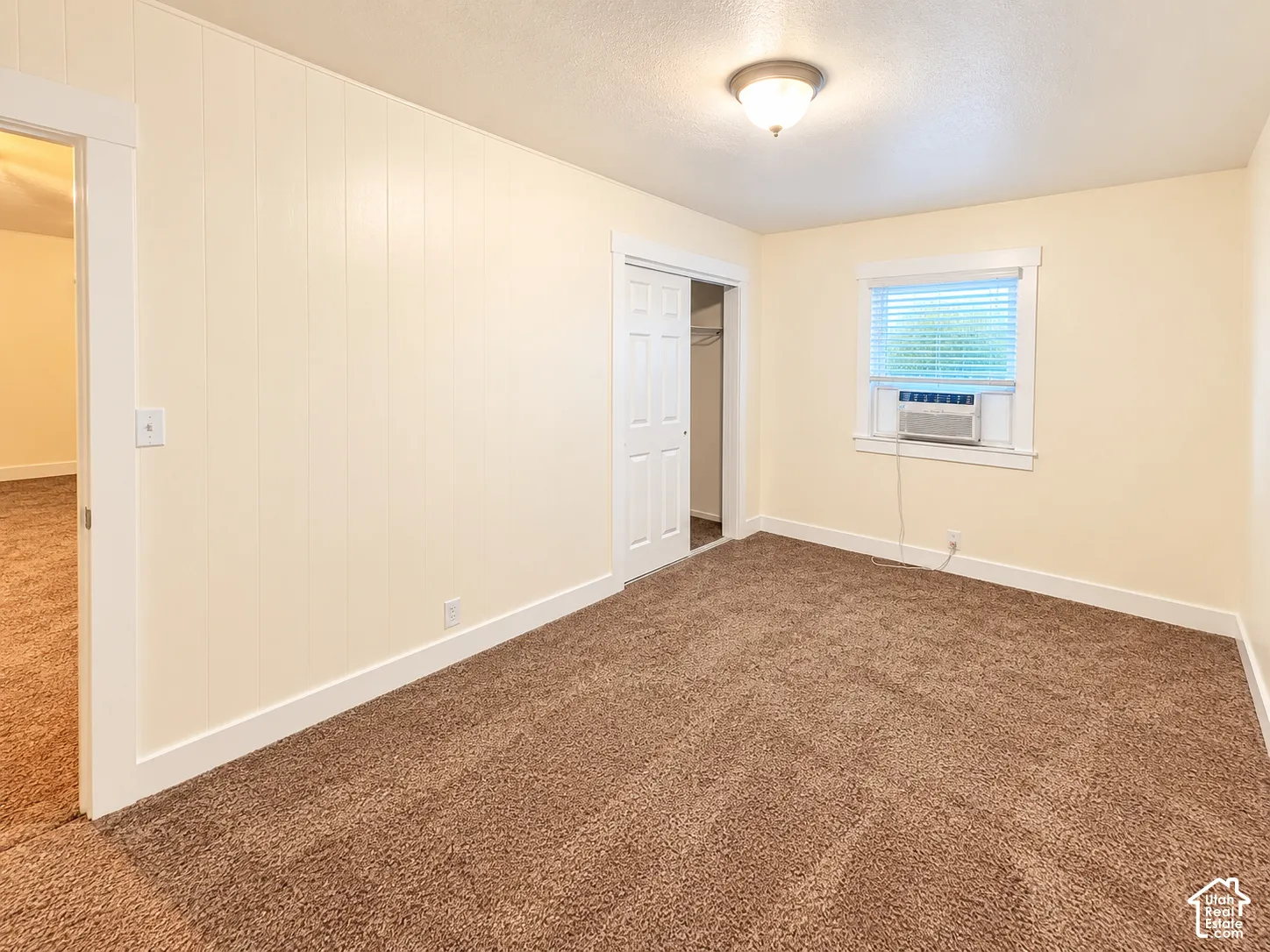 Room featuring wall-to-wall carpeting, vertical paneled wall detailing, a single-door closet with overhead shelving, and a dual-pane window with white trim