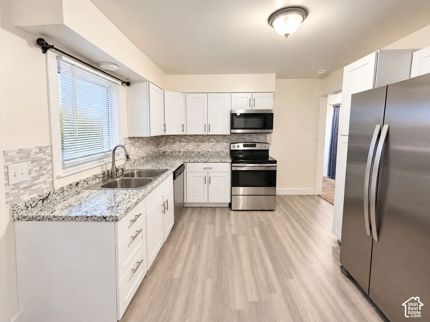 Kitchen featuring white cabinetry, stone-patterned countertops, a tile backsplash, stainless steel appliances, and wood-finish flooring