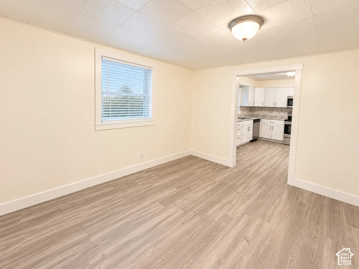 Interior room featuring wood-finish flooring, a double-hung window with blinds, and a textured tile ceiling