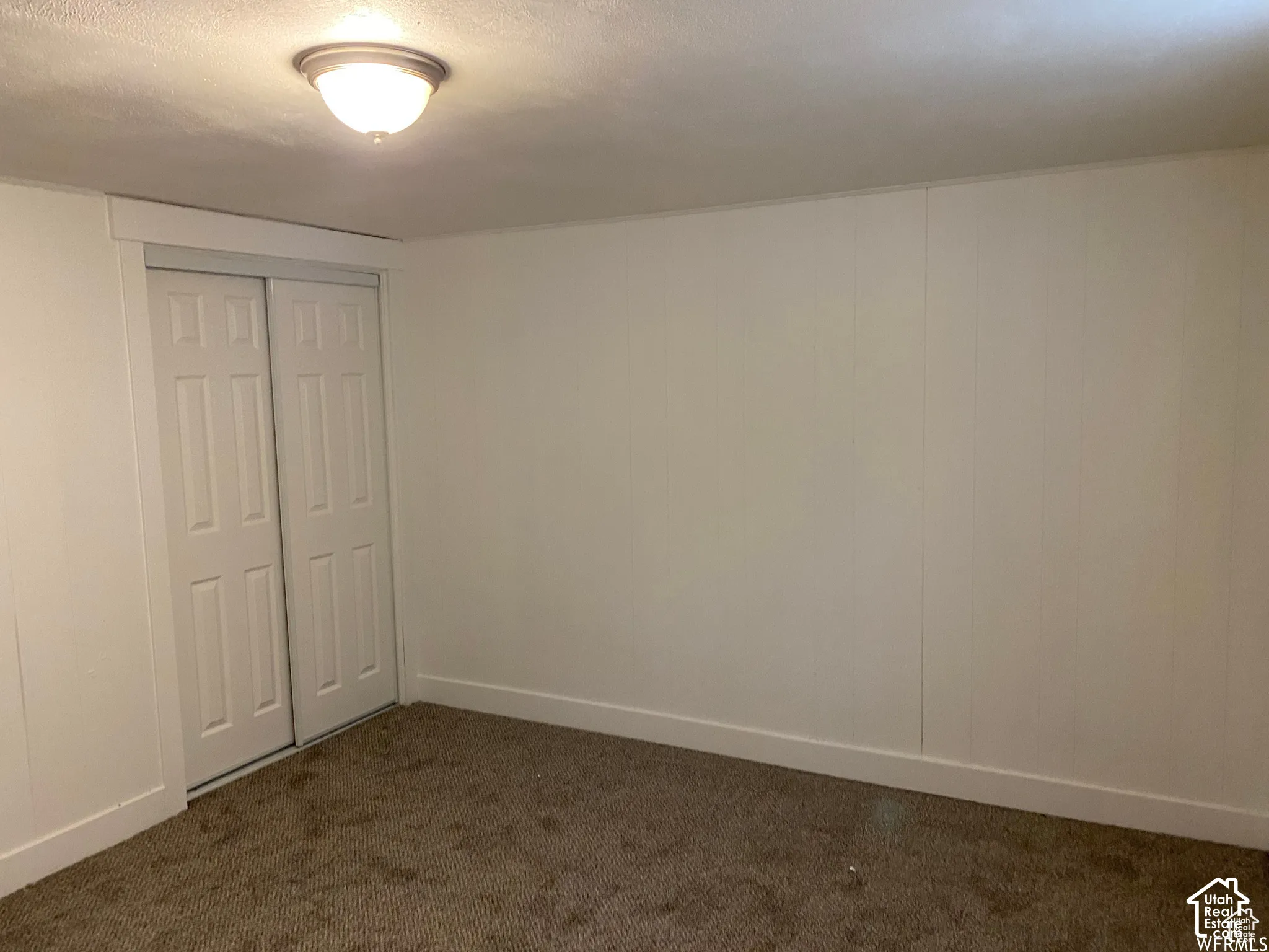 White bi-fold closet doors, wall-to-wall carpeting, and a flush mount ceiling light fixture