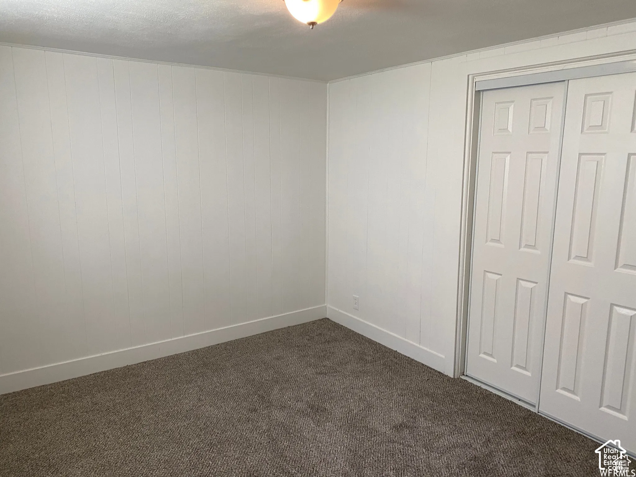 Vertical wall paneling, flush-mount ceiling light, paneled bi-fold closet doors, and textured carpet flooring