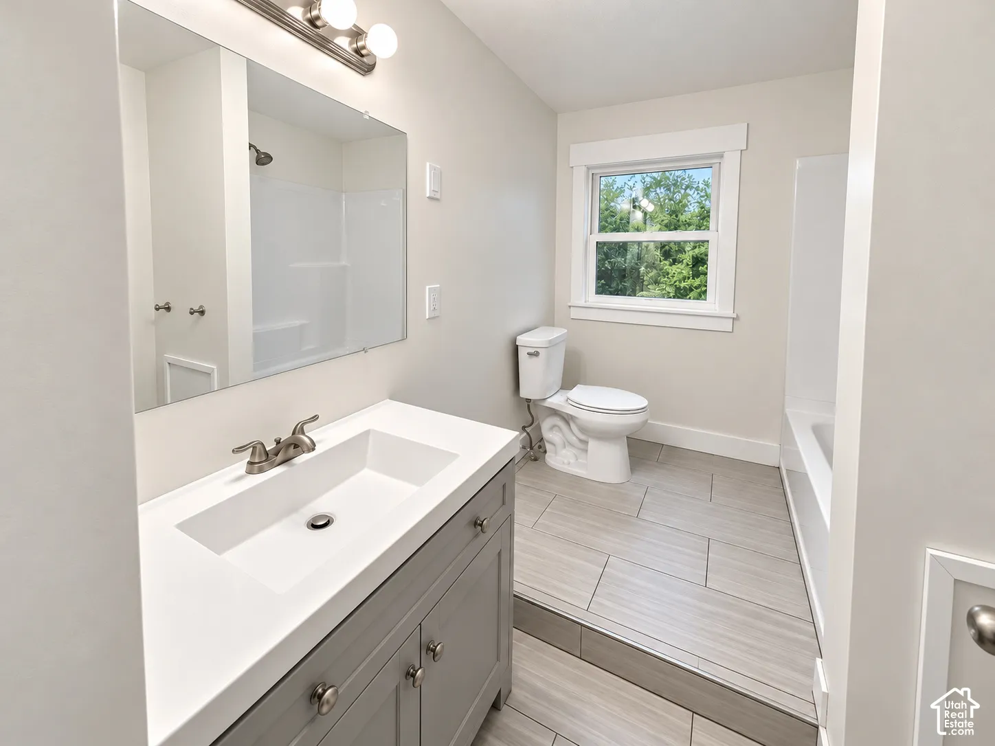 Bathroom featuring a vanity with a rectangular sink, quartz countertop, large wall-mounted mirror, ceramic tile flooring, and a shower-tub combination