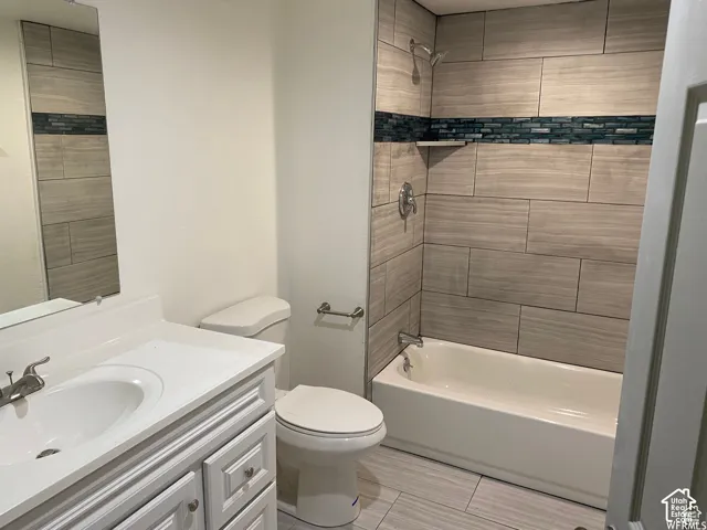 Bathroom featuring a built-in tub with shower, tiled surround, vanity with an integrated sink, and wood-finish flooring