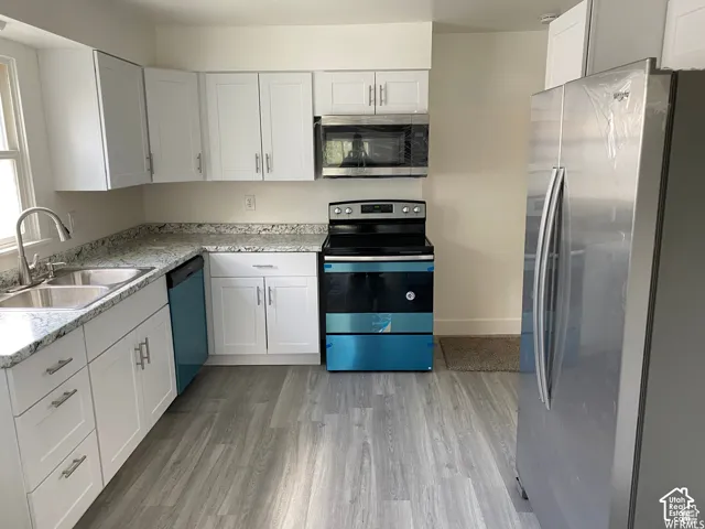 Contemporary kitchen featuring white cabinetry, light-toned countertops, stainless steel appliances, and wood-finish flooring