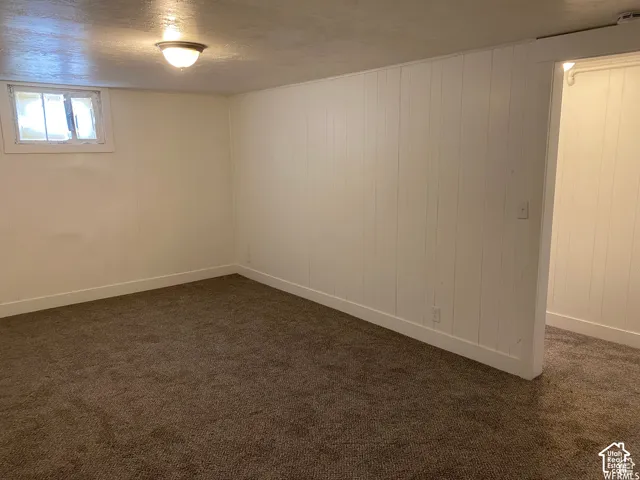 Recessed window with security bars, vertical paneling accent wall, flush-mount ceiling light fixture, and textured carpeting