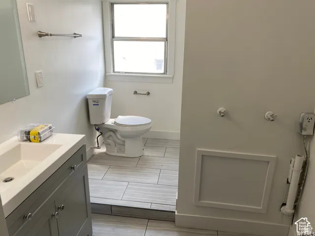 Bathroom featuring a single window, white toilet, tile flooring, and a vanity with an integrated sink