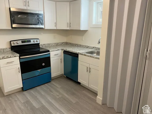 Kitchen featuring white cabinetry, light-toned countertops, a stainless steel microwave, a built-in dishwasher, and wood-finish flooring