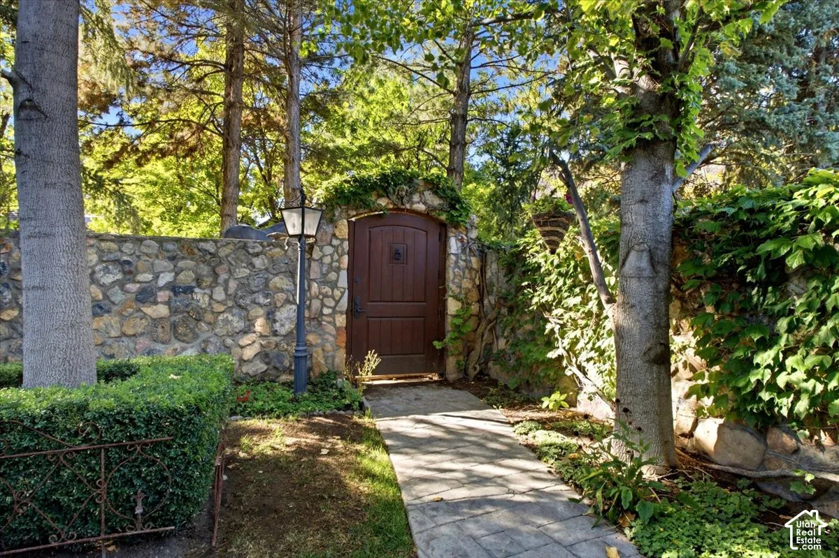 Stone-clad wall with an arched wooden entry door, accented by a decorative outdoor lantern and lush perimeter landscaping