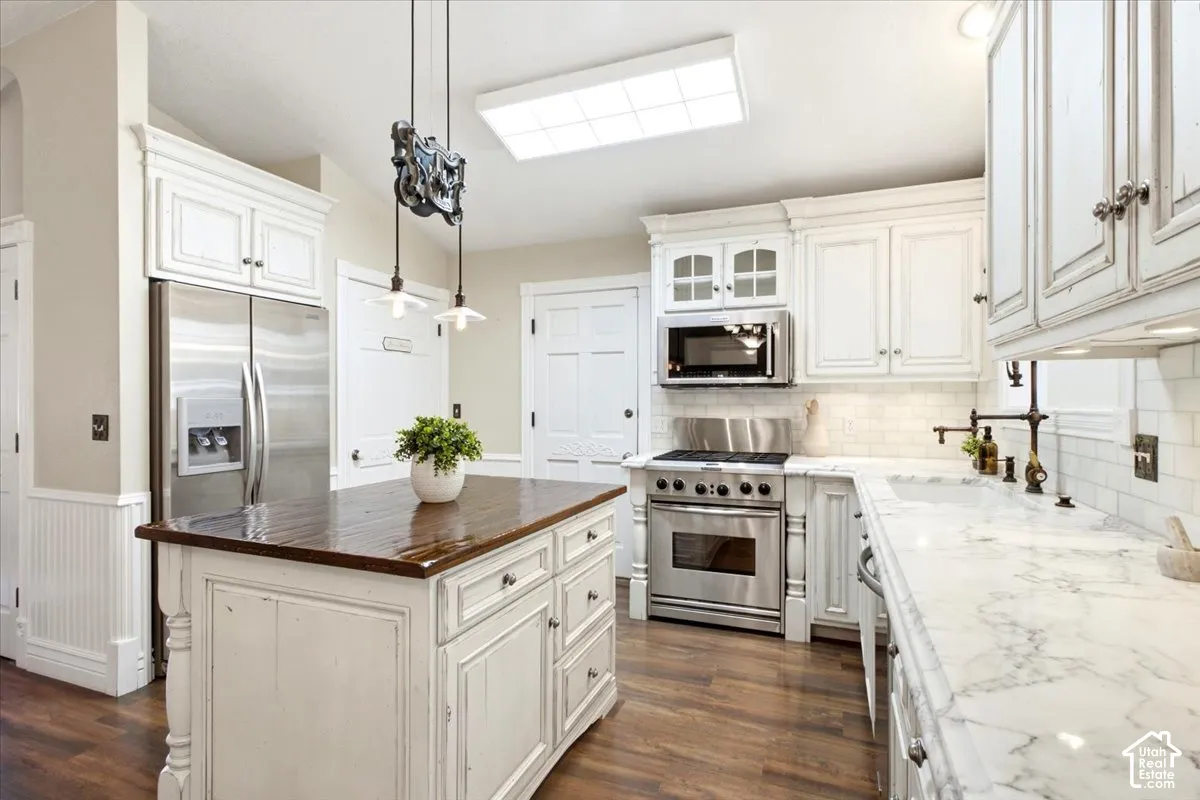 Gourmet kitchen featuring white cabinetry, wood-finish flooring, a center island with a wood countertop, a stainless steel refrigerator, and built-in stainless steel appliances