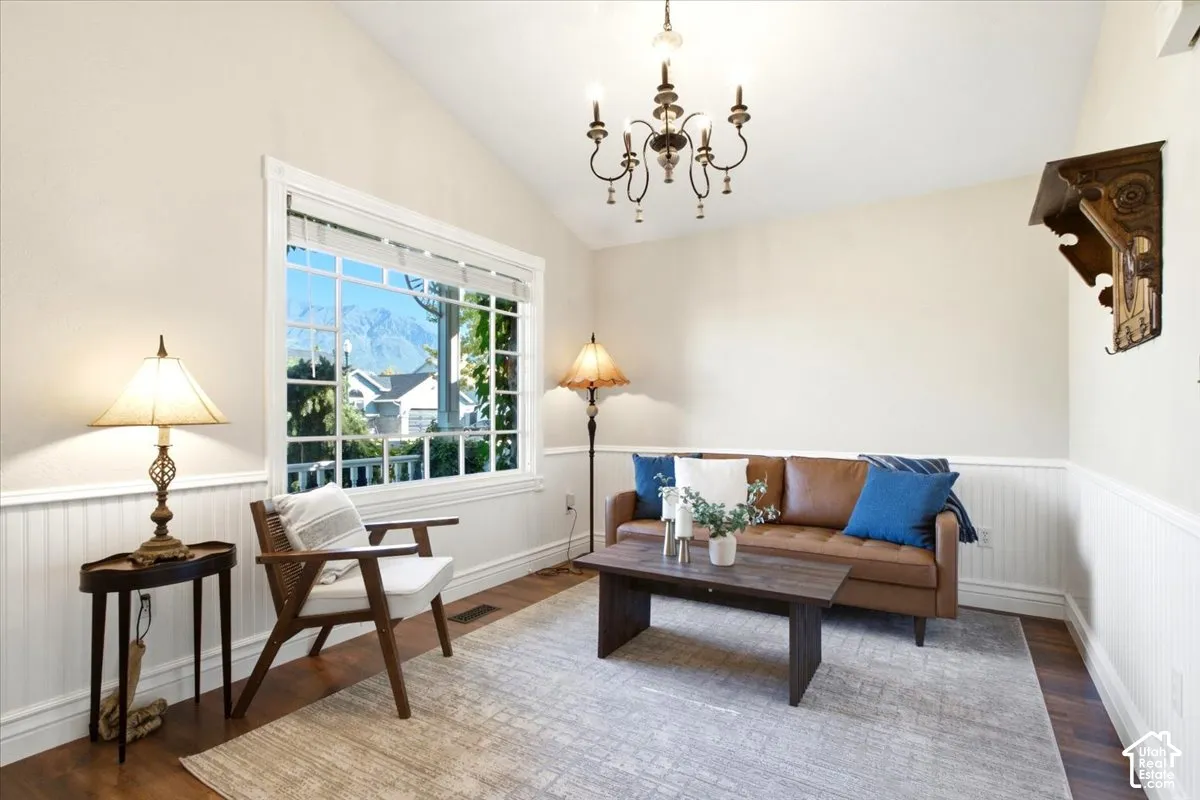 Vaulted ceiling with an ornate chandelier, large window with grid pattern, wood-finish flooring, and wainscoting paneling
