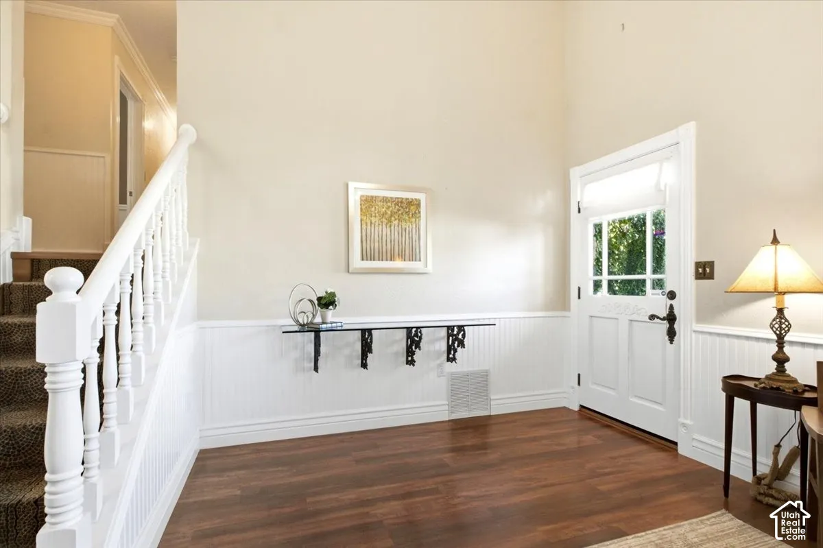 Wood-finish flooring, white wainscoting, a staircase with white balusters, and a glass-paneled entry door