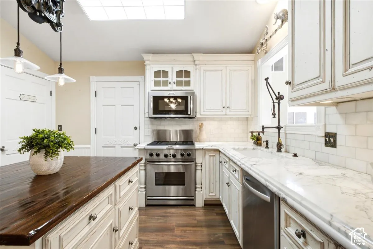 Wood-finish flooring with white cabinetry, stainless steel appliances, and a skylight