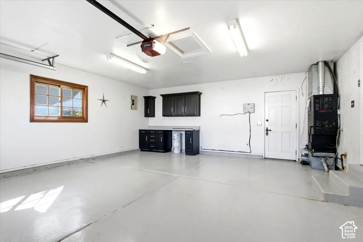 Attached garage featuring a light-colored epoxy floor, built-in cabinetry, a single window with wood-frame trim, and fluorescent lighting fixtures