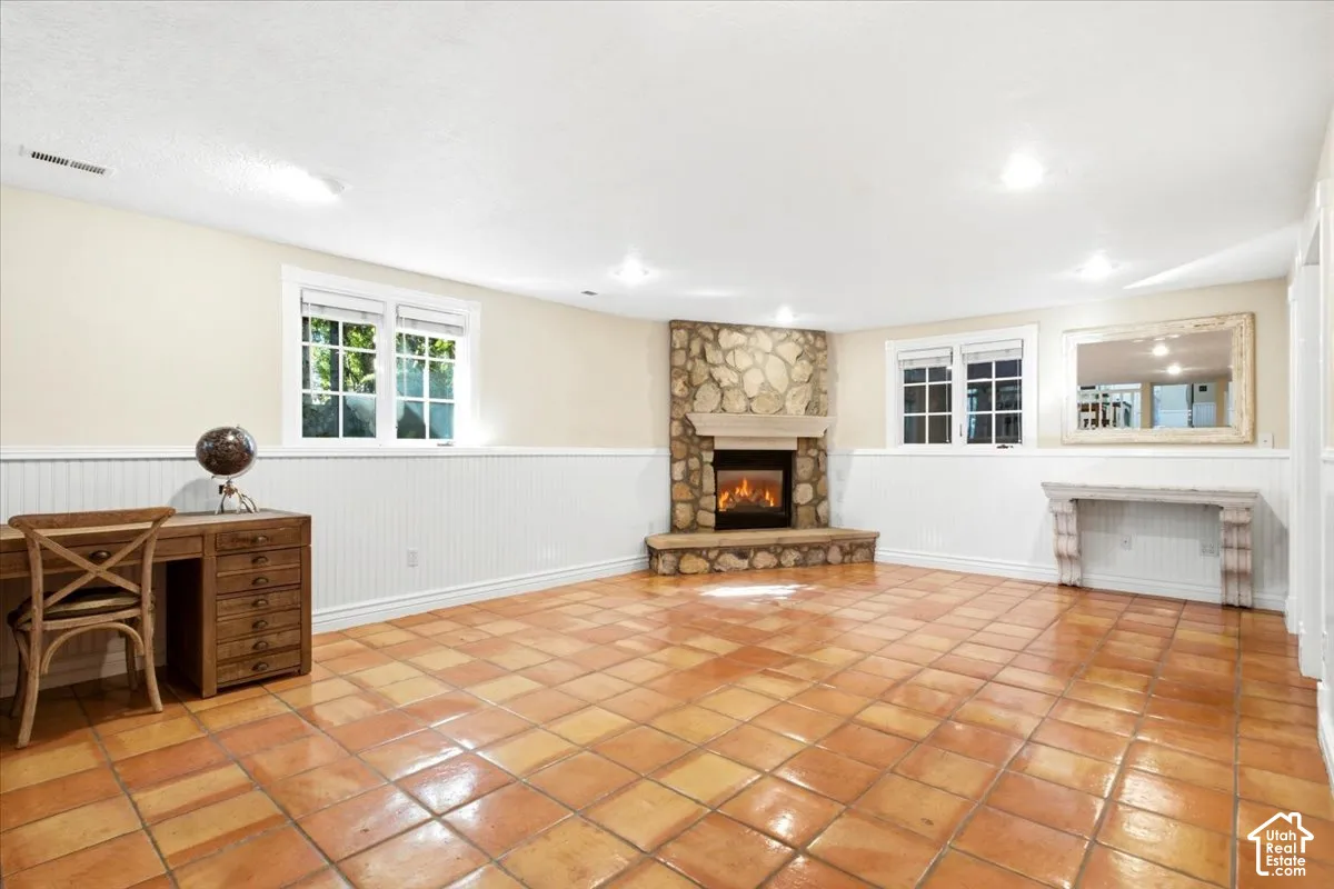Corner stone fireplace with hearth, terra cotta tile flooring, white beadboard paneling, recessed lighting, and multiple windows
