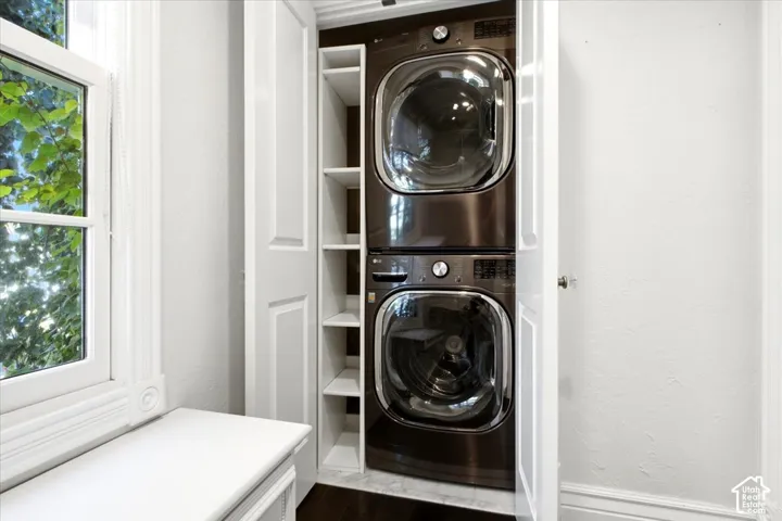 Stacked laundry appliances with built-in shelving, white paneled doors, and a window with white trim