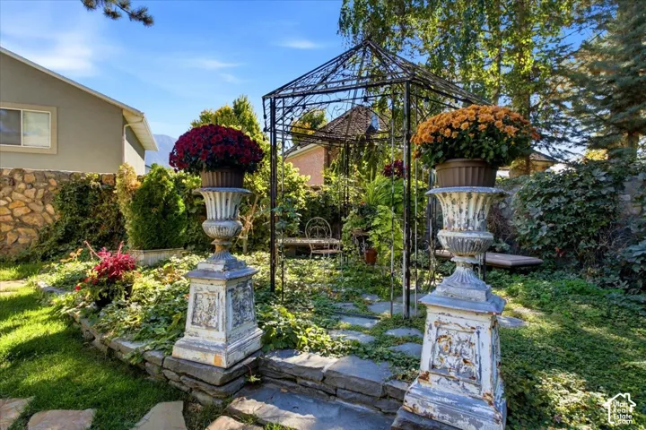 Landscaped garden featuring a metal gazebo, stone retaining wall, and decorative urns